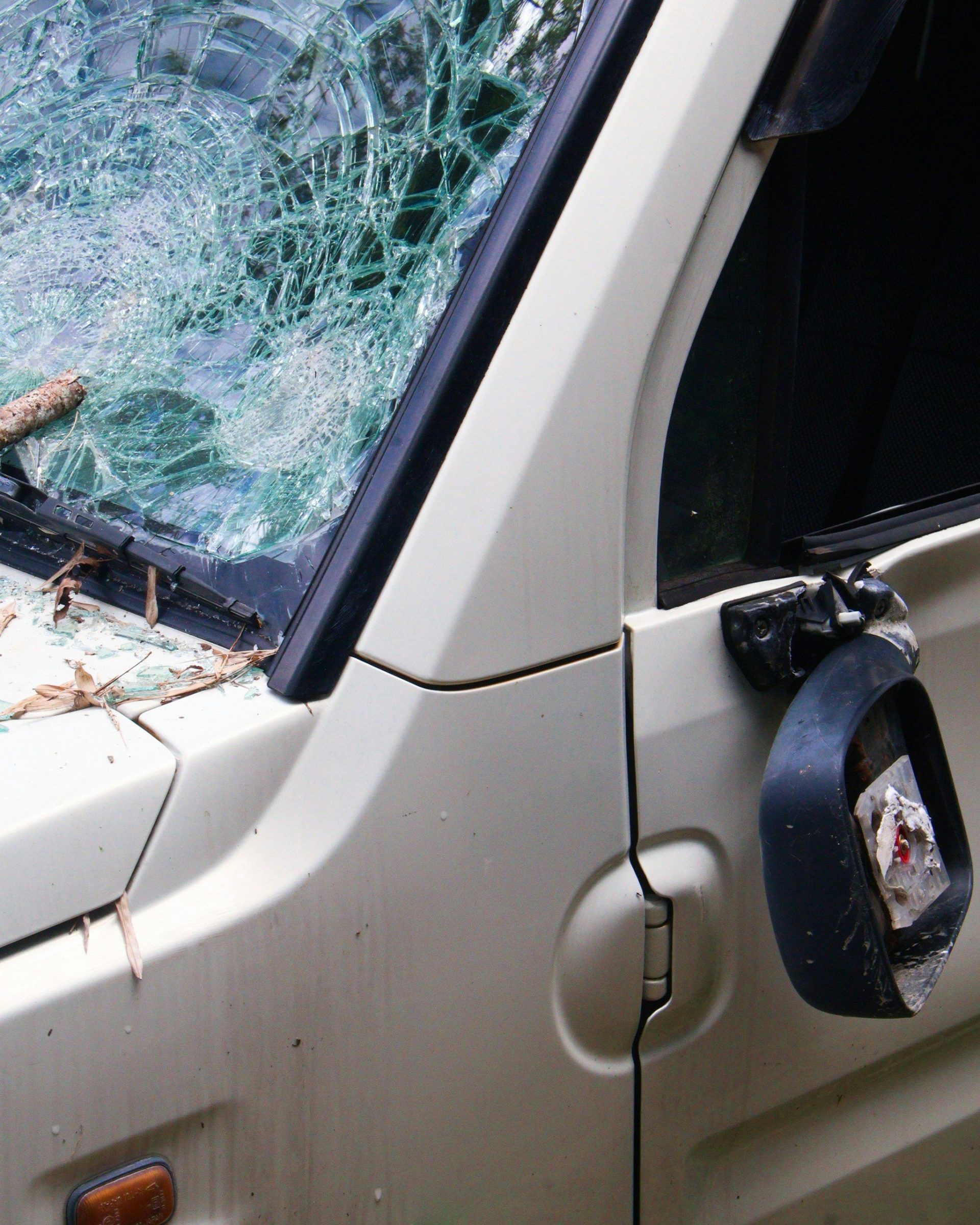 Beschädigtes Auto mit zersplitterter Windschutzscheibe und kaputtem Außenspiegel.
